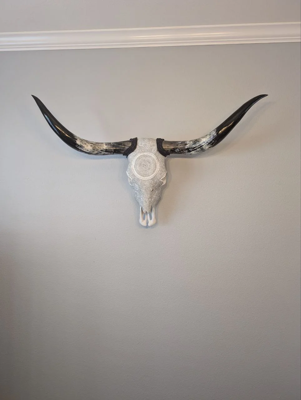 Silver-white artwork with a circular pattern and sweeping horns on a soft neutral wall