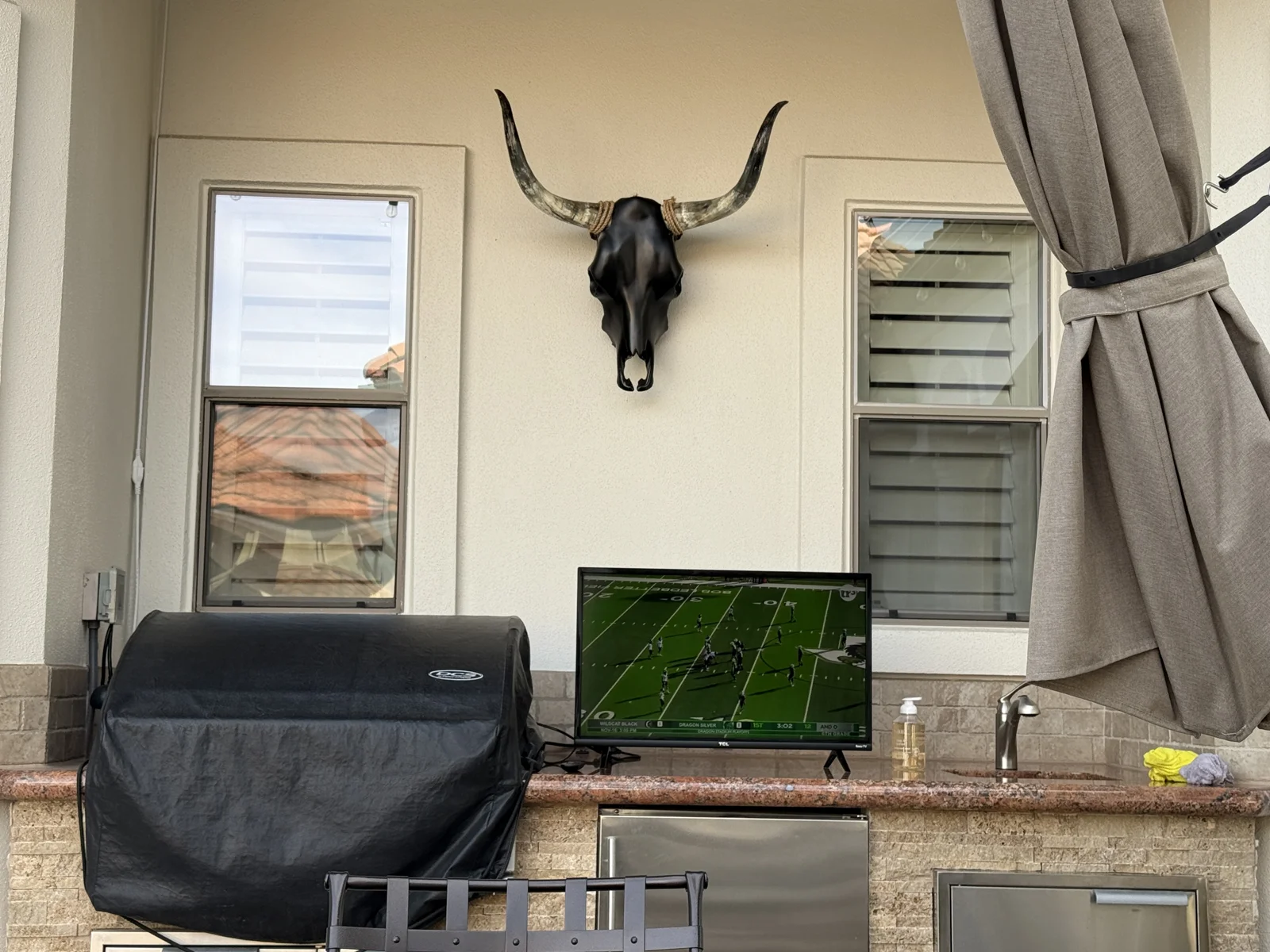 Black skull artwork with natural horns between two windows above a client's outdoor kitchen counter