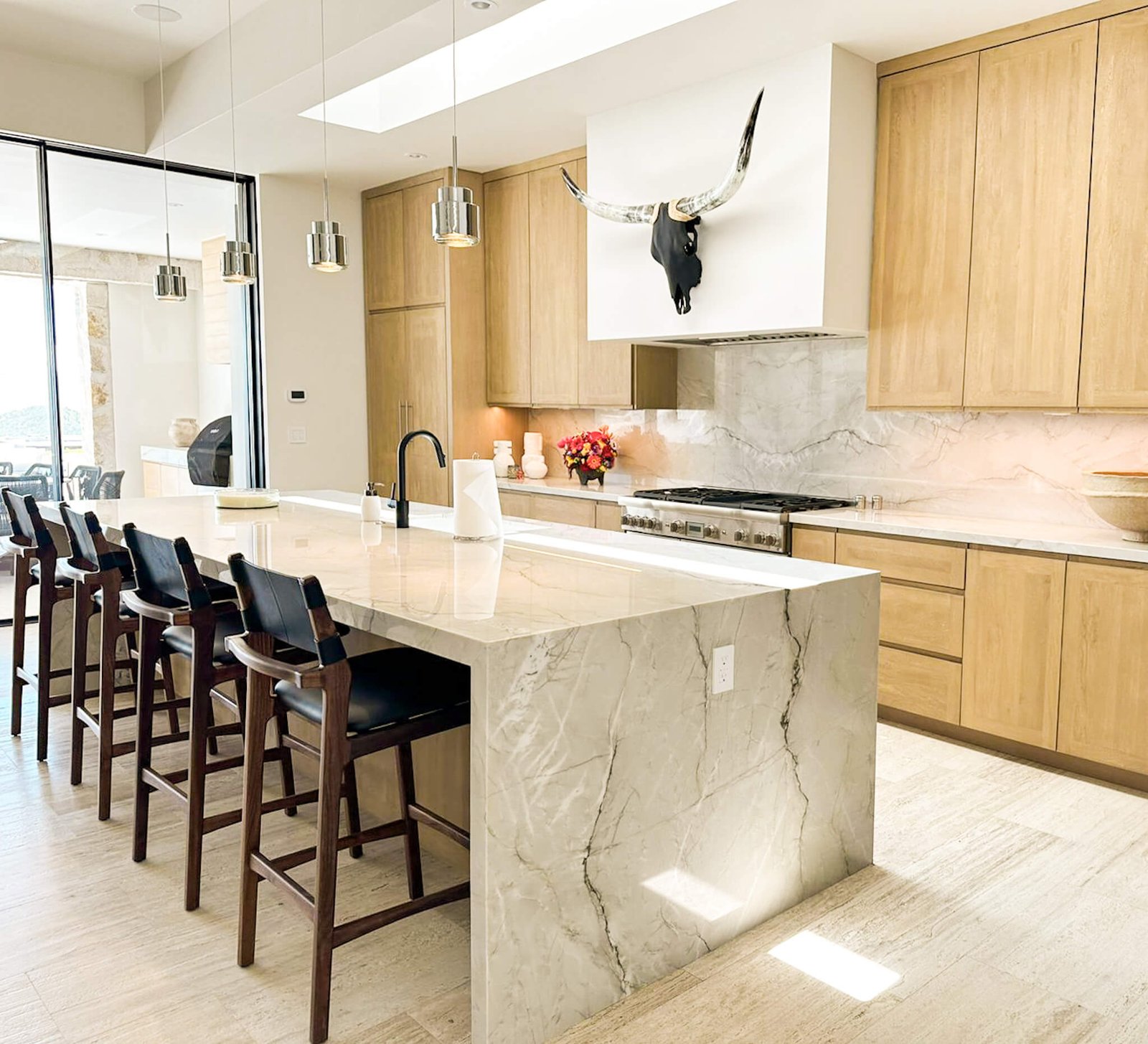 Cabokero artwork above the range hood in a bright kitchen with a marble island.