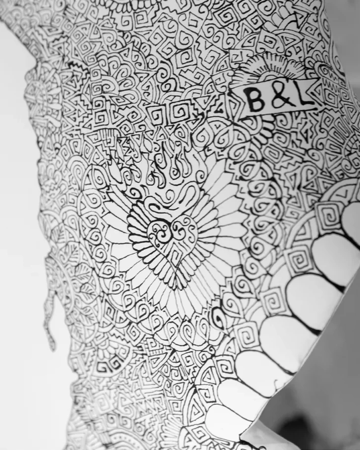 Two initials integrated into fine black linework near a sculpted eye socket